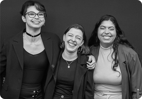 Imagem das 3 sócias em frente a um fundo preto. A foto está em preto e branco e, ao redor de cada uma, existem elementos relacionados a cartas de taror desenhados no estilo doodle